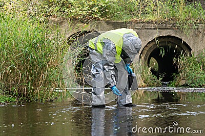 A specialist in a protective suit holds a suitcase with equipment in his hands and measures the level of water pollution in the Stock Photo