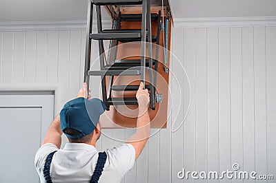A specialist in uniform folds the attic ladder after installation Stock Photo