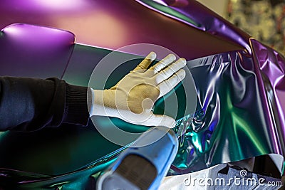A specialist in wrapping a car with chameleon-colored vinyl film in the process of work. Stock Photo