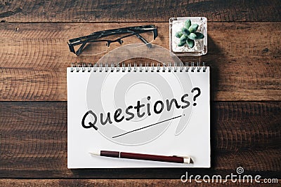 Spectacle, cactus, pen and notebook with QUESTIONS word on wooden table Stock Photo