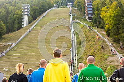 Spectators on sport event cheering for conmpetitors running upwards on ski jump. Editorial Stock Photo