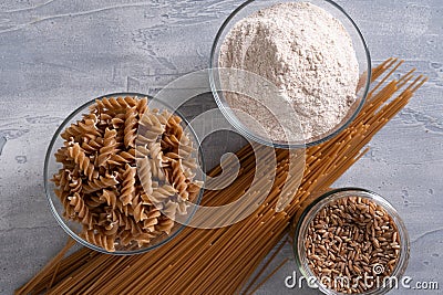 Spelt pasta, spelt grain and whole grain spelt flour in bowl and jar. Top view. Stock Photo