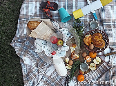 Spend time with children.A small picnic on the lawn in the yard. A food basket with a loaf, milk and homemade cakes on a plaid. Stock Photo