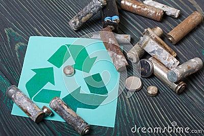 Spent finger-type batteries coated with corrosion. Waste recycling sign. They lie on brushed pine boards painted in black and Stock Photo