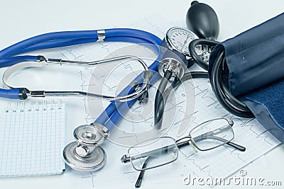 Sphygmomanometer on the working table of a cardiologist. Tonometer, electrocardiogram and notepad for records. Stock Photo