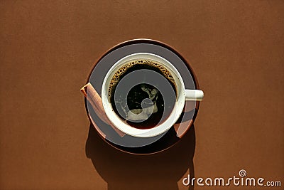Spicy black coffee concept. Ceramic cup, saucer, cinnamon on chocolate brown background. Monochrome horizontal poster for cafe, Stock Photo