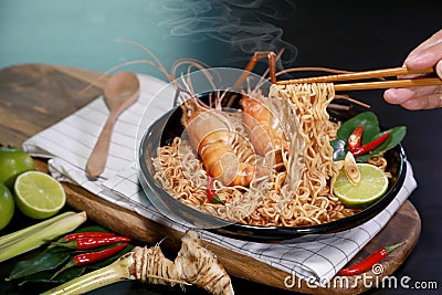 Spicy instant noodles soup and rivers shrimp with hand and chopsticks, on black table background. Tom Yum Kung name in Thailand Stock Photo