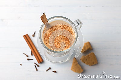 Spicy warming tea with milk in a glass cup and cinnamon sticks, cloves, with gingerbread cookie Stock Photo