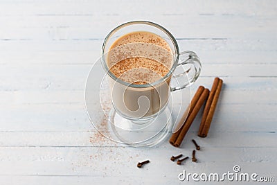 Spicy warming tea with milk in a glass cup with cinnamon sticks and cloves on light gray blue background Stock Photo