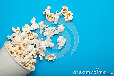 Spilled popcorn from a paper bucket or a cup on a blue background Stock Photo