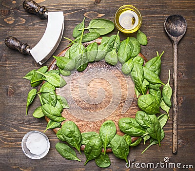 Spinach leaves have been laid out around a circular chopping board, with herbs and salad spoon, knife and salad, frame, space for Stock Photo