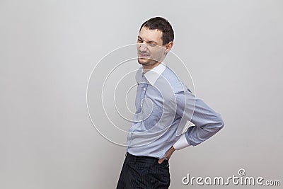 Spine, back or kidney pain. Profile side view portrait of handsome bristle businessman in classic blue shirt standing and holding Stock Photo