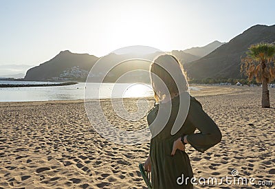 Spiritual adolescent in green dress admire the sunset and the sea town on a hill in Tenerife. Blonde romantic woman look the Stock Photo