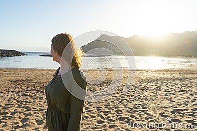 Spiritual adolescent in green dress admire the sunset and the sea town on a hill in Tenerife. Blonde romantic woman look the Stock Photo
