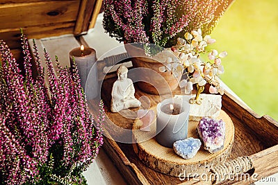 Spiritual home balcony decor with heather flowers, candlelight flame, crystal geodes, crystal wire tree and small Buddha figurine. Stock Photo