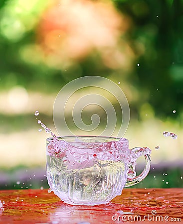 Splash of cool fresh water with ice cube in transparent glass cup in the table outoors in summer day. Stock Photo