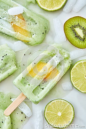 Splashes of fruit ice cream on a stick and pieces of ice, lime and kiwi on a gray background.Summer dessert lolly with a Stock Photo