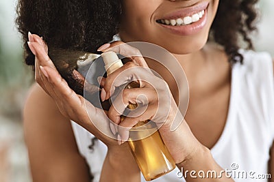 Split Ends Treatment. Smiling Black Woman Spraying Essential Oil On Curly Hair Stock Photo