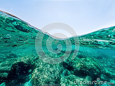 Split underwater view of a rocky sea bed under a blue sky Stock Photo