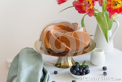 Sponge cake with icing, fresh blueberries and tulips bouquet on the table. Side view, copy space. Bakery, recipe, pastry Stock Photo