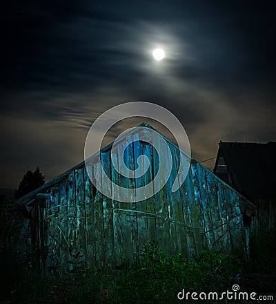 A spooky old wooden barn at night illuminated with full moon Stock Photo