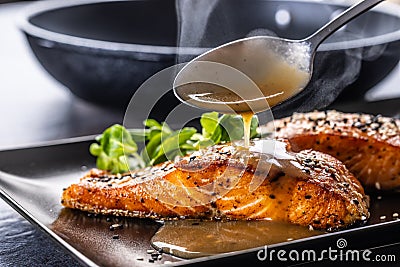 The spoon finishes the portion by pouring a demiglas sauce over the salmon fillets Stock Photo