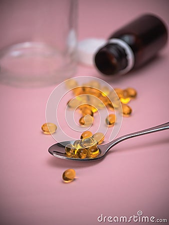 Spoon with fish oil pills. Cod Liver Oil Capsules on spoon on pink background. Stock Photo