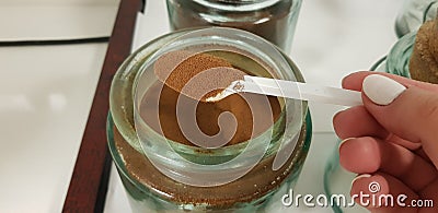 Spoon with instant coffee powder in female fingers over big glass can with coffee Stock Photo