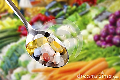 Spoon with pills, dietary supplements on vegetables background Stock Photo