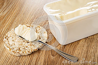 Spoon with soft cheese on crispbread, white container with cream cheese on table Stock Photo