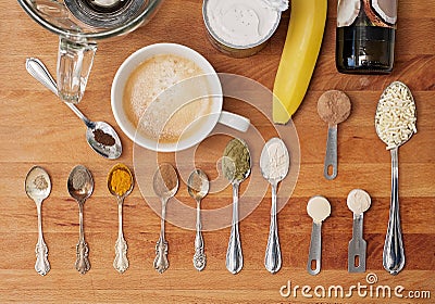 Spoons and spices to prepare a super coffee: a cup and a blender on a wooden chopping board with banana, MCT oil, turmeric, black Stock Photo