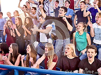 Sport fans hands up and singing on tribunes. Stock Photo