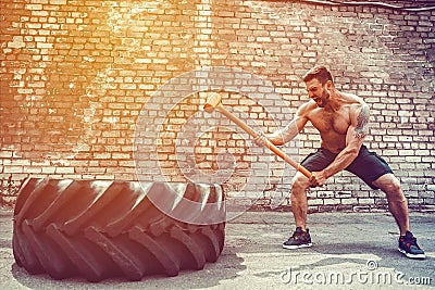 Sport Fitness Man Hitting Wheel Tire With Hammer Sledge Crossfit Training. Stock Photo