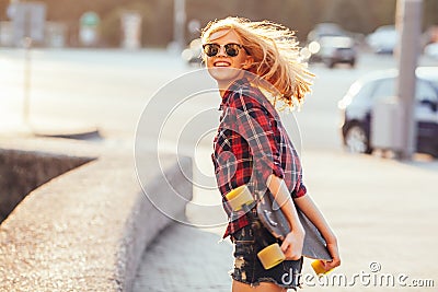 Sport happy girl posing in summer with skateboard. Stylish lucky hipster woman with colorful longboard in sunset in Stock Photo