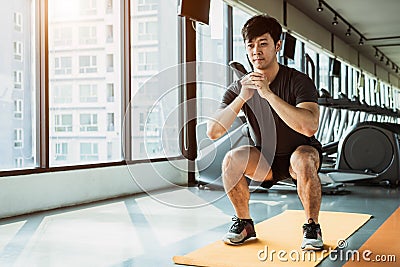 Sport man doing squat posture on yoga mat in fitness gym at condominium in urban. People lifestyles and Sport workout concept Stock Photo