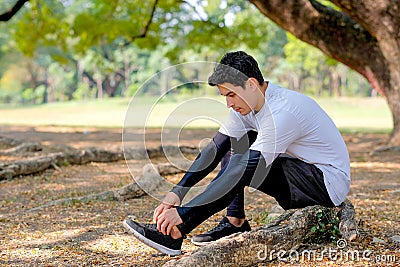 Sport man with white shirt and black legging tie shoelace under branch of big tree during exercise in the garden with copy space Stock Photo