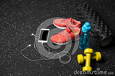 Sport shoes, dumb-bells, pilates mat, blue bottle, and phone with headphones on a black background. Sport concept. Stock Photo