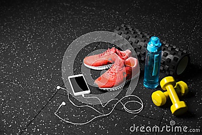 Sport shoes, dumb-bells, pilates mat, blue bottle, and phone with headphones on a black background. Training concept. Stock Photo