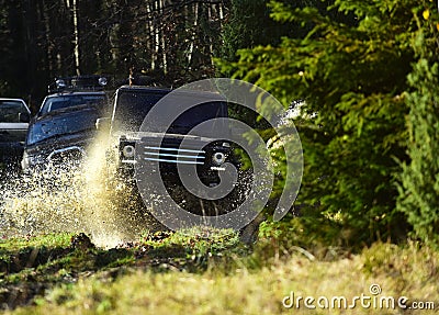 Sport utility vehicle or SUV crossing puddle with splash. Offroad race on fall nature background. Rallying, competition Stock Photo