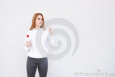 Sporting a white background with a bottle of water in her hands, looking sideways and listening to music Stock Photo