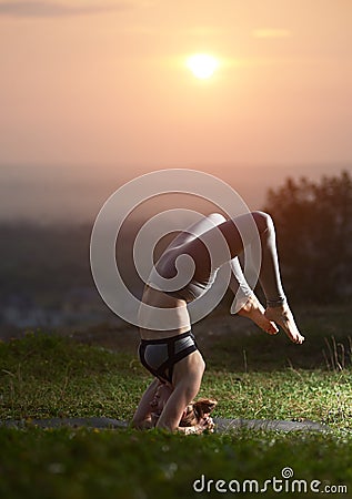 Attractive slim young woman doing yoga exercises outdoors on background of beautiful sky. Stock Photo