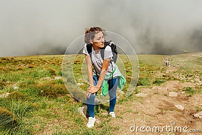 Woman hiker climbing on mountain surrounded with clouds in Carpathians. Tired traveler with backpack resting Stock Photo