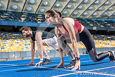 sportive young male and female sprinters in start position on running track Stock Photo