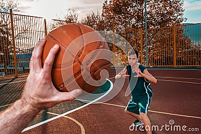 Sports and basketball. A man`s hand holds a basketball for submission. In the background, a teenager in a blur preparing to catch Stock Photo