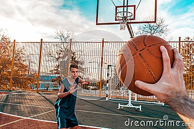 Sports and basketball. A man`s hand holds a basketball for submission. In the background, a teenager preparing to catch a ball. Stock Photo