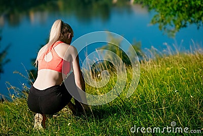 Sports girl blonde in a red T-shirt sat down to tie laces on sneakers in a park near the river. Stock Photo