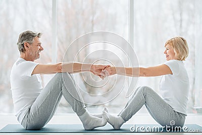 Sports and healthy lifestyle.Sporty middle aged couple sitting on the mat in the white fitness gym and doing stretching while Stock Photo