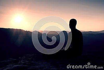 Sportsmann hiker in black sportswear sit on mountain top and take a rest. Tourist watch down to morning misty valley. Stock Photo