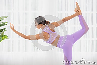In sportswear, an Asian lady works out. Natarajasana, Lord of the Dance Pose, is being prepared. Asana for balancing and back Stock Photo