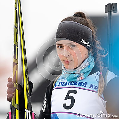 Sportswoman biathlete Knyazeva Elizaveta with skis in hands and rifle behind her after skiing and rifle shooting. Junior Editorial Stock Photo